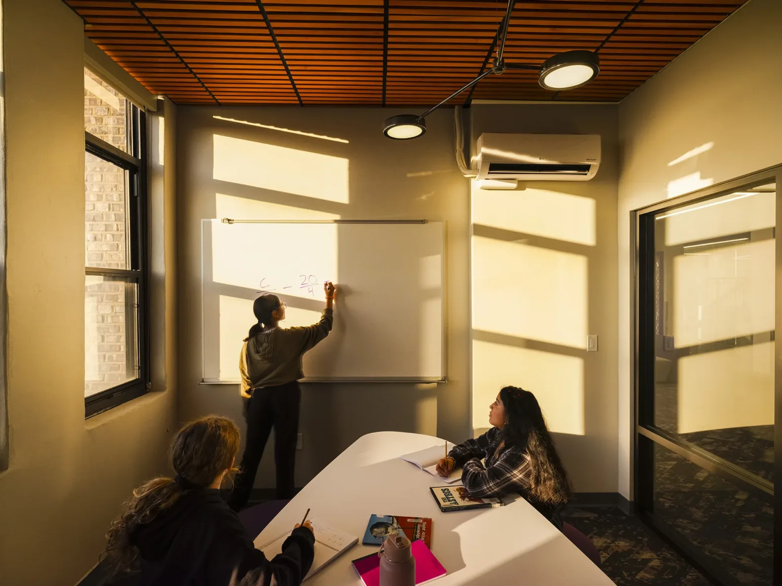 Students studying in a classroom while one student draws on the whiteboard and light shines through