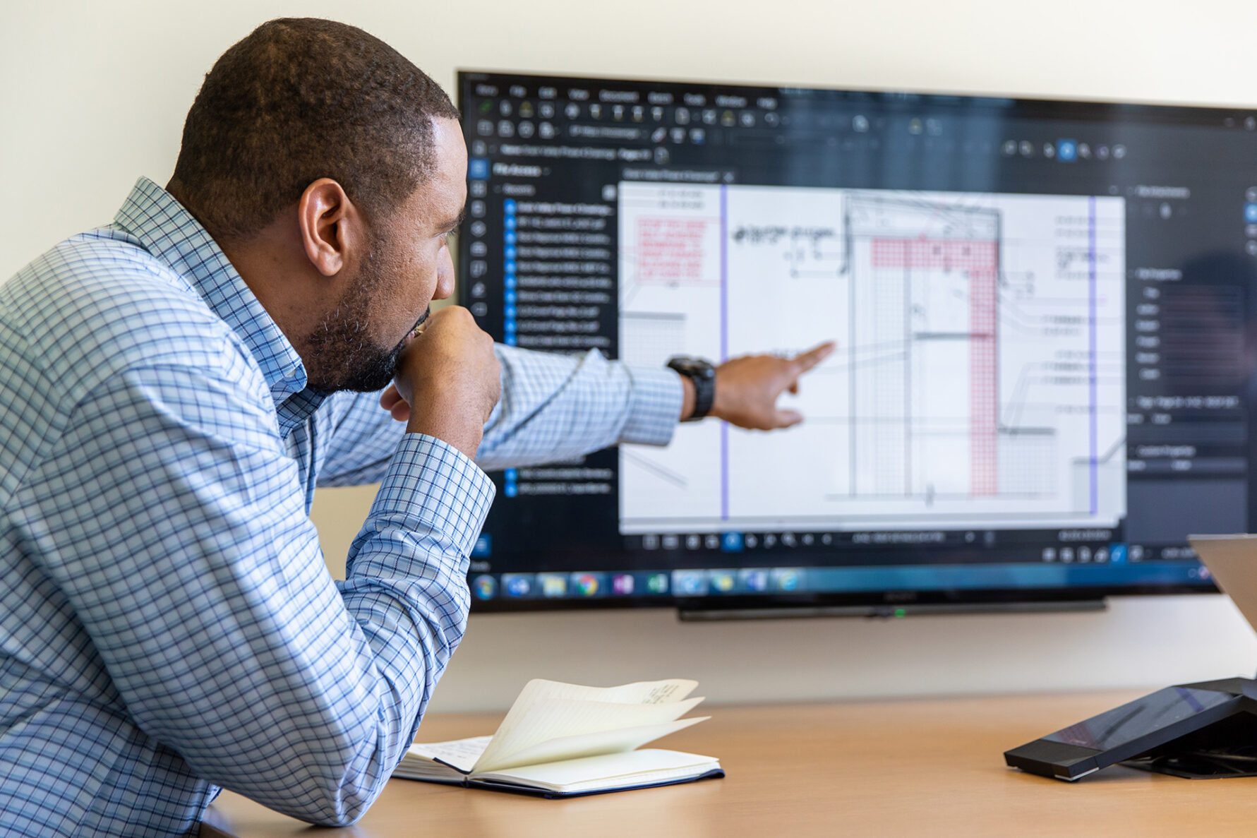 McCownGordon associate pointing at a construction estimate from the preconstruction process on a tv screen