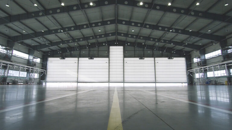 Roller shutter door and concrete floor inside factory building for industrial background. Airplane in front of half opened door to hangar. The open door of the hangar.