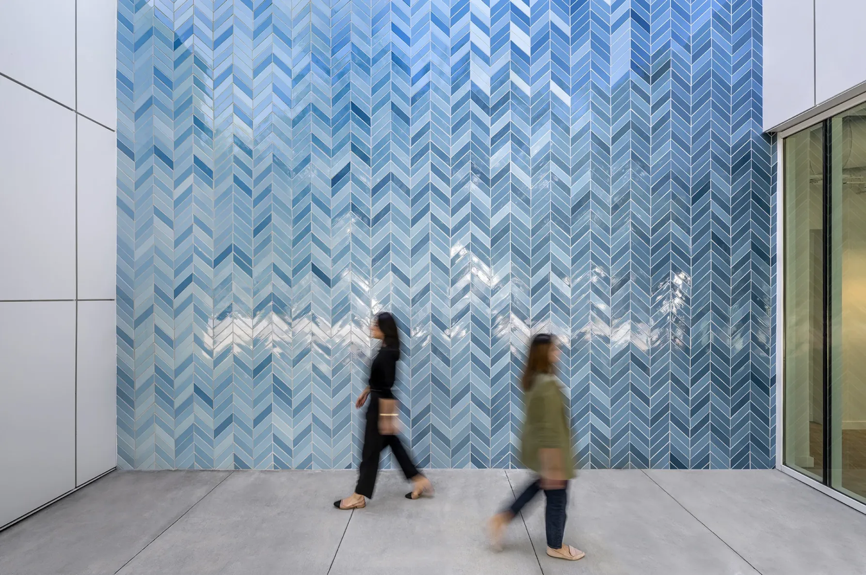 Two girls walking by a blue tile wall at White Rhino Coffee and Conference Center in Dallas Texas